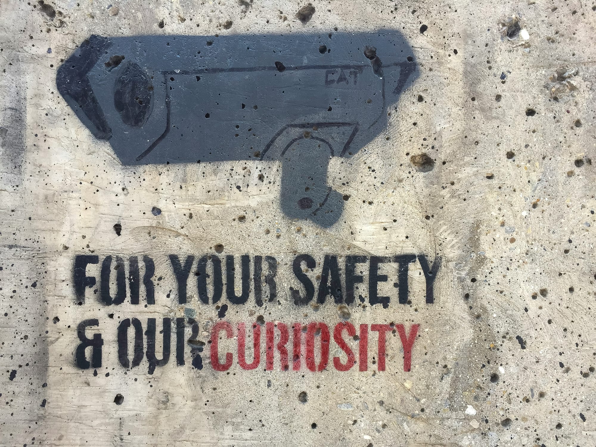 A Grafitti of a sourveillance camera with the text 'FOR YOUR SAFETY & OUR CURIOSITY'